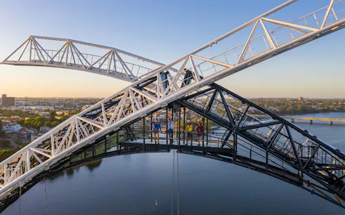 People climbing bridge arch with city and river view, daytime.