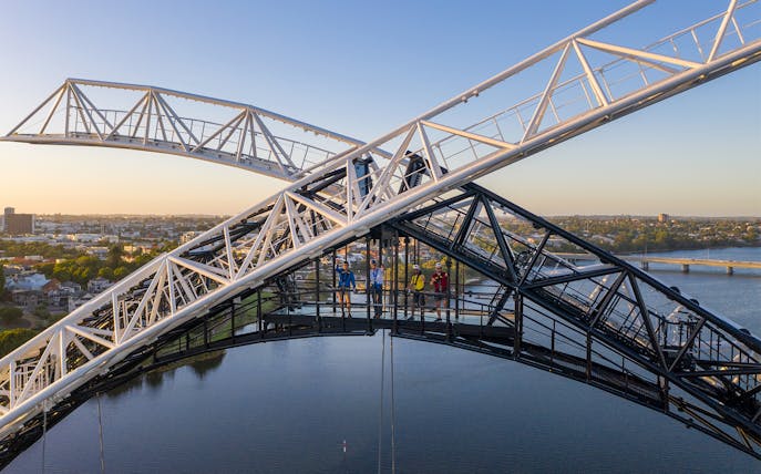 People climbing bridge arch with city and river view, daytime.