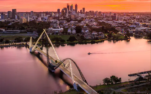 Twilight view of a bridge over a river with city skyline in the background.