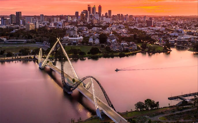 Twilight view of a bridge over a river with city skyline in the background.