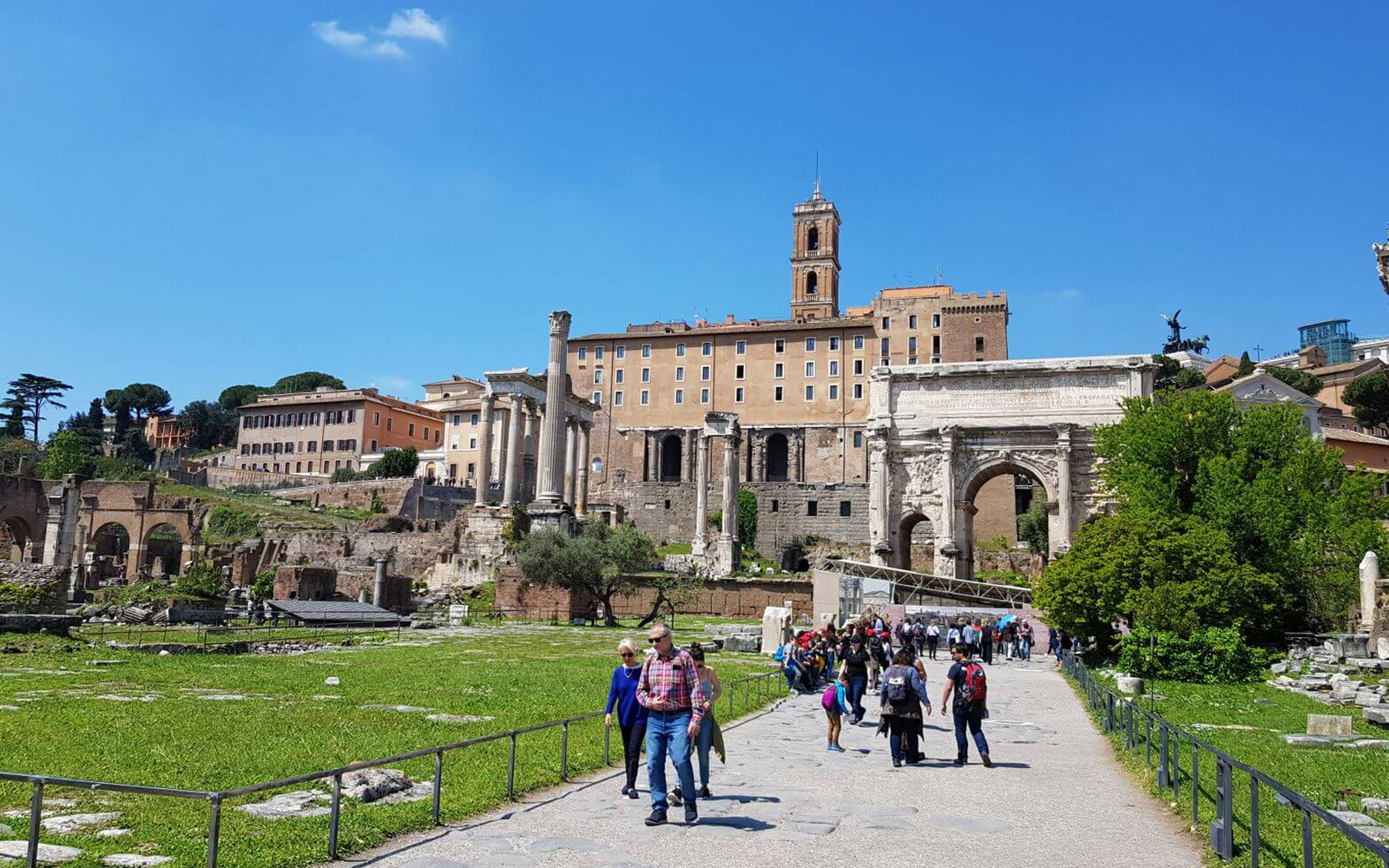 Visitors walking through the Roman Forum with ancient ruins and buildings in the background.