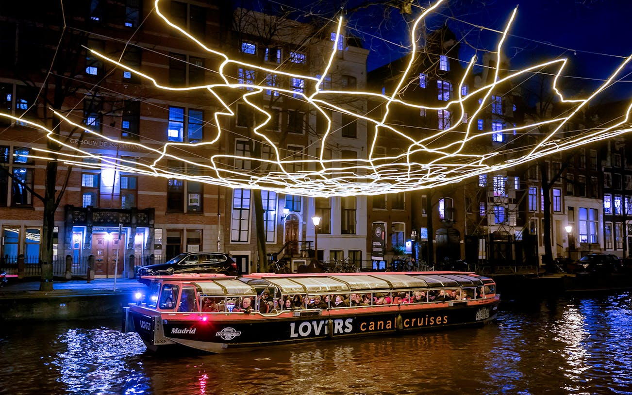 Semi-open boat cruising under illuminated art at Amsterdam Light Festival.