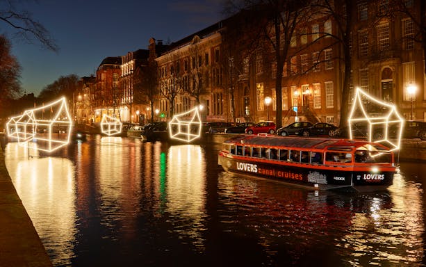 Semi-open boat cruising through Amsterdam Light Festival canal with illuminated art installations.