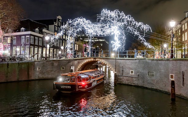 Semi-open boat cruise under illuminated bridge at Amsterdam Light Festival.