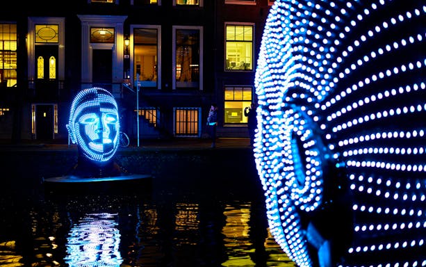 Illuminated face sculptures at Amsterdam Light Festival during semi-open boat cruise.