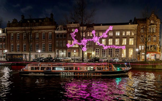 Amsterdam canal cruise boat passing illuminated art installation during Light Festival.