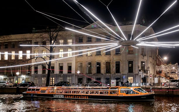Amsterdam canal cruise boat under festival lights at night.