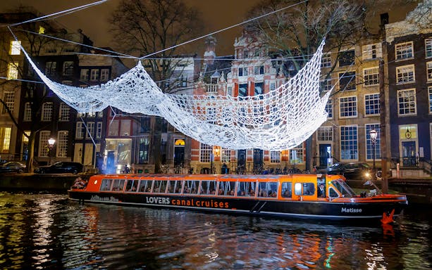 Amsterdam canal cruise boat under illuminated art installation during Light Festival.
