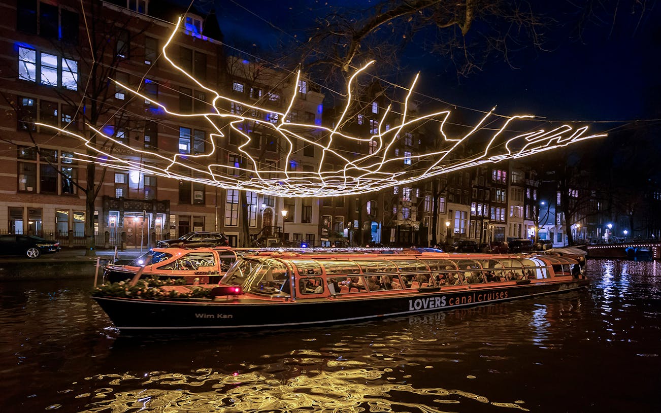 Amsterdam canal cruise boat under illuminated light installation during Light Festival.