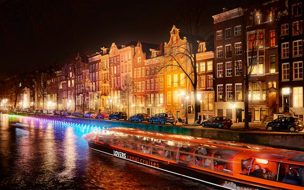 Amsterdam canal cruise boat passing illuminated buildings during Light Festival.