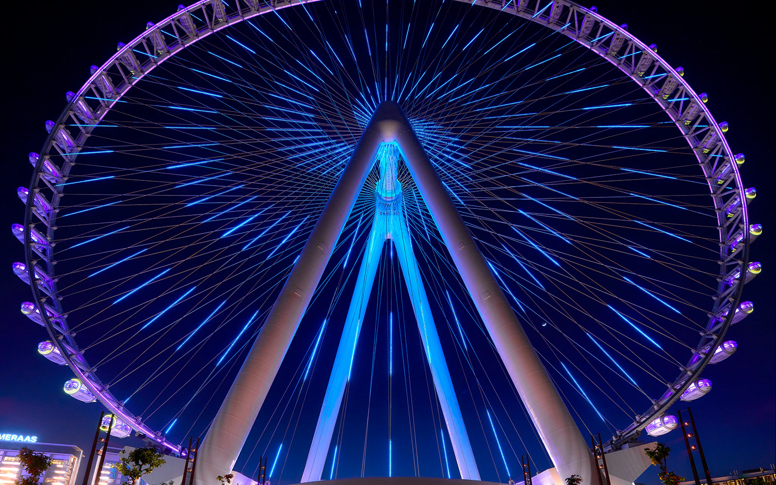 Ain Dubai Ferris wheel illuminated at night, Dubai skyline in background.