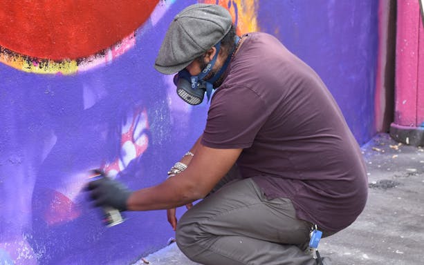 Artist spray painting a colorful mural on Belleville street art tour.