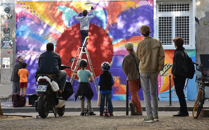 Artist painting colorful mural during Belleville Street Art Tour, Paris.