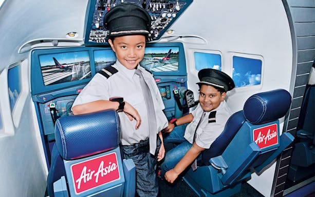 Children in pilot uniforms inside a flight simulator at KidZania Kuala Lumpur.