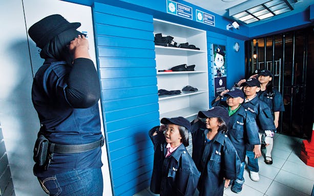 Children in police uniforms saluting an instructor at KidZania Kuala Lumpur.