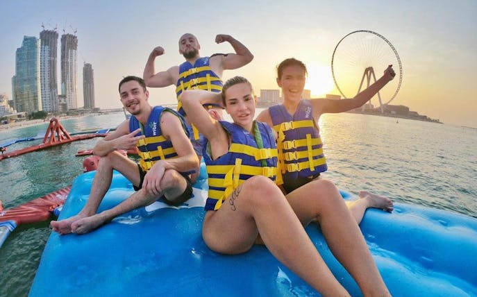 Group enjoying Aqua Fun water park in Dubai with city skyline and Ferris wheel in background.