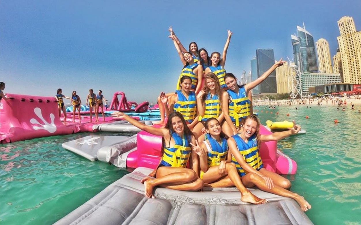 Group enjoying inflatable water park at Aqua Fun Dubai with city skyline in background.