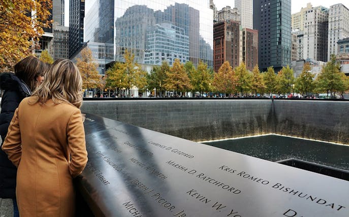Visitors at the 9/11 Memorial in New York City, viewing engraved names around the reflecting pool.