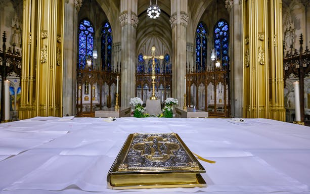 Altar view inside St Patrick's Cathedral, New York, with ornate Bible and stained glass windows.