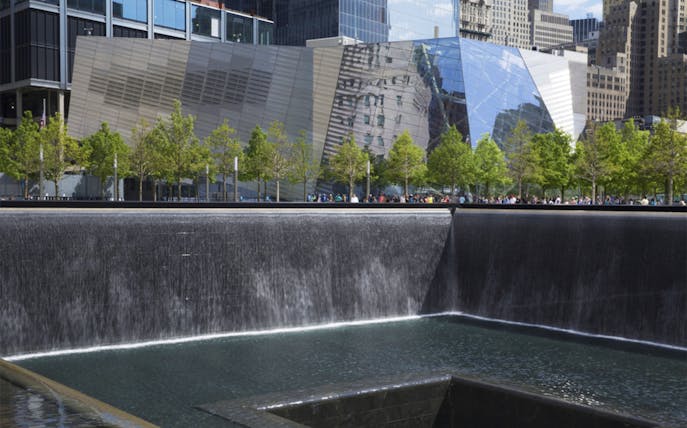 Ground Zero 9/11 Memorial waterfall with surrounding trees and modern buildings in New York City.