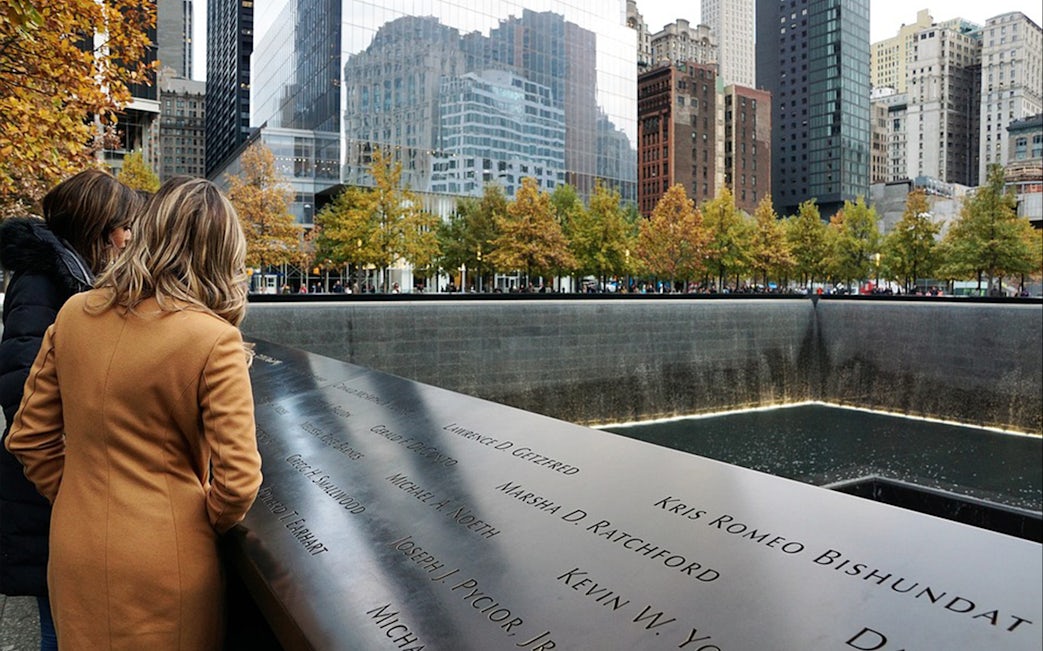 Visitors at the 9/11 Memorial in New York City, viewing engraved names at the reflecting pool.