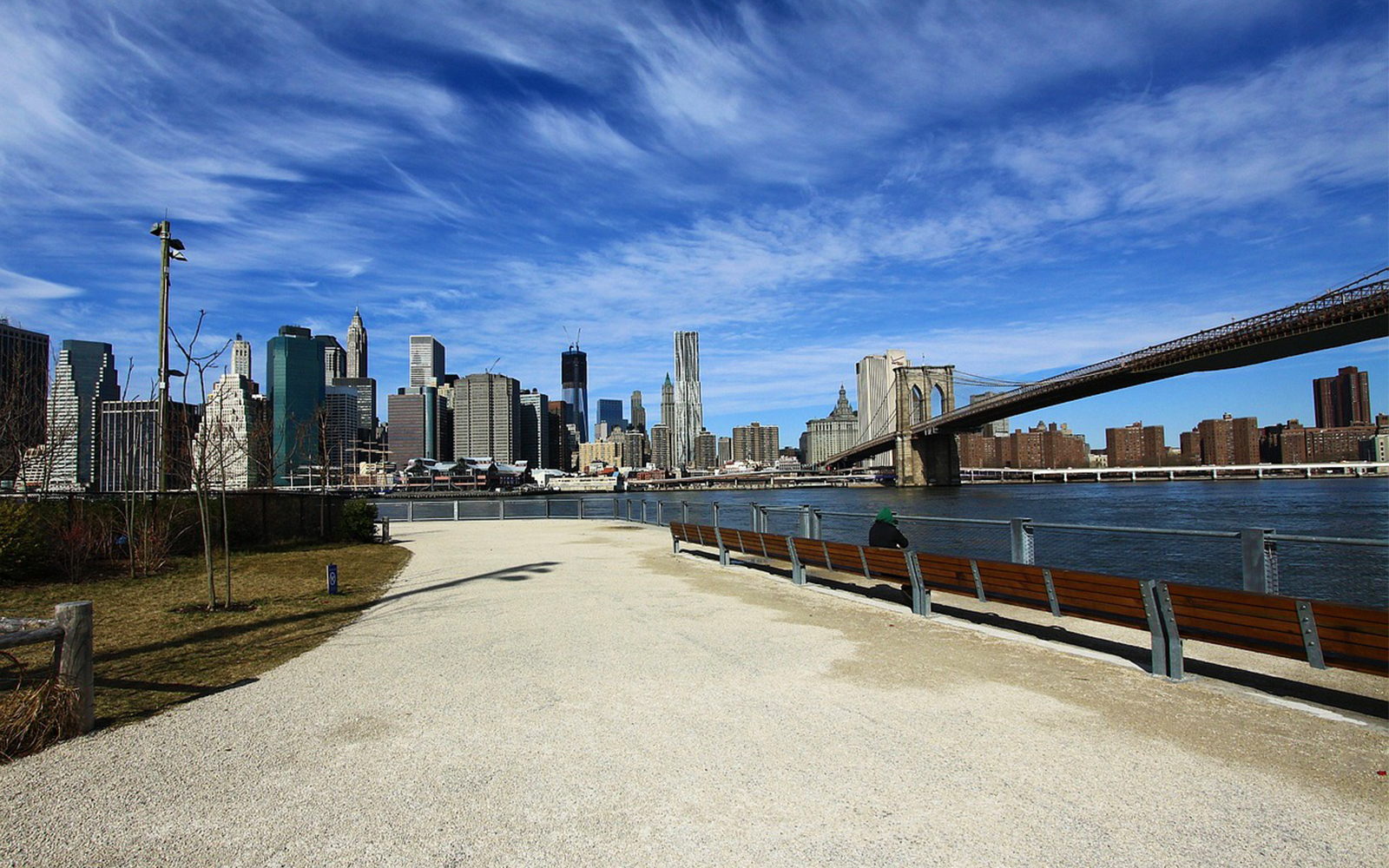 Brooklyn Bridge and Manhattan skyline viewed from a riverside path.
