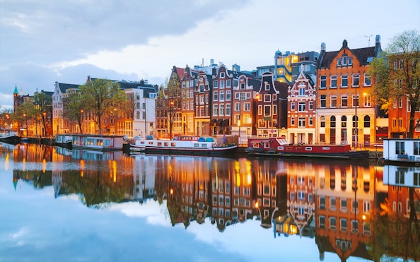 Amsterdam canal houses and boats reflecting in the water during a cruise.