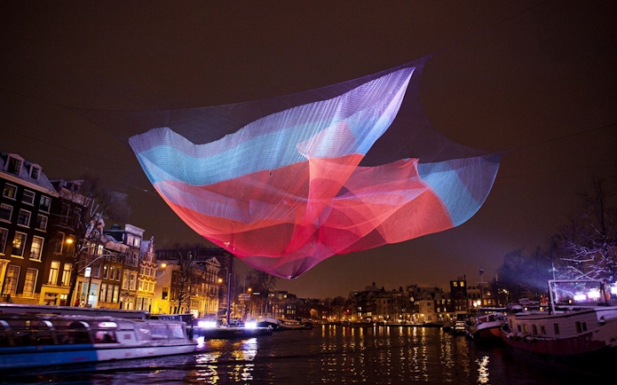 Colorful light installation over Amsterdam canal during Light Festival.