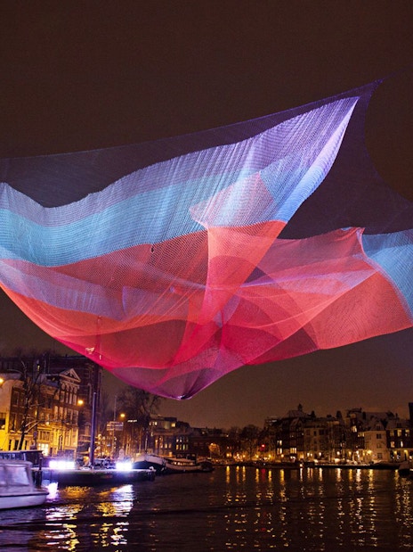 Colorful light installation over Amsterdam canal during Light Festival.