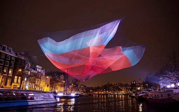 Colorful light installation over Amsterdam canal during Light Festival.