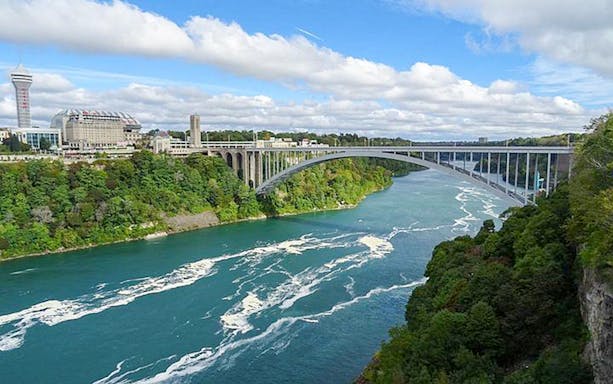 Niagara Falls USA tour view of Rainbow Bridge spanning the river with lush greenery.
