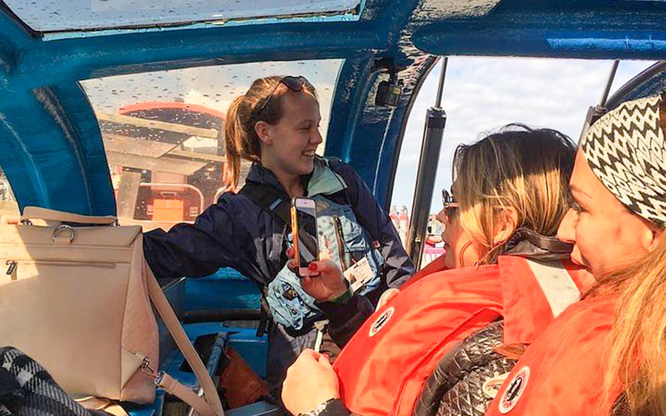Tourists in a jet boat on the USA side of Niagara Falls, wearing life jackets and taking photos.