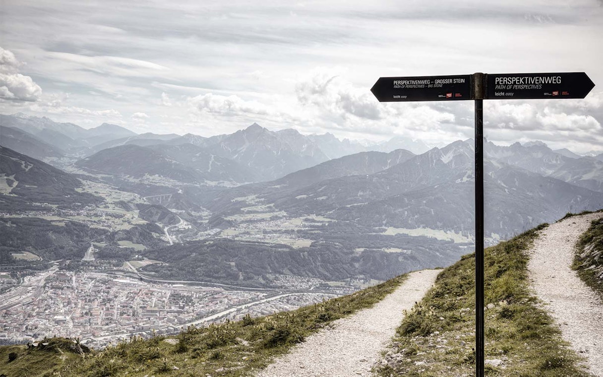 Mountain view from Path of Perspectives in Innsbruck, Austria, with signpost and city below.