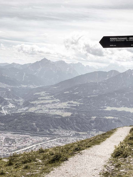 Mountain view from Path of Perspectives in Innsbruck, Austria, with signpost and city below.