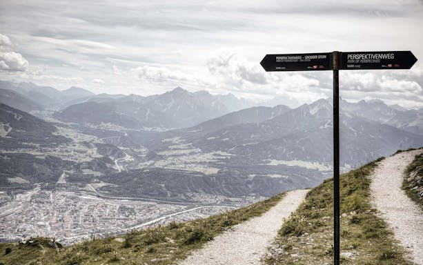 Mountain view from Path of Perspectives in Innsbruck, Austria, with signpost and city below.