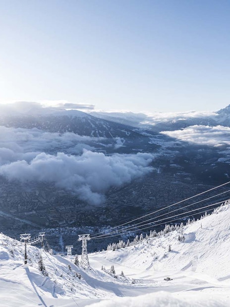 Cable car ascending snowy mountain with Innsbruck city view.