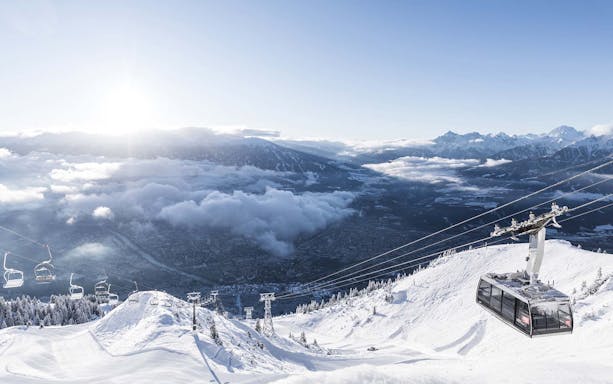 Cable car ascending snowy mountain with Innsbruck city view.