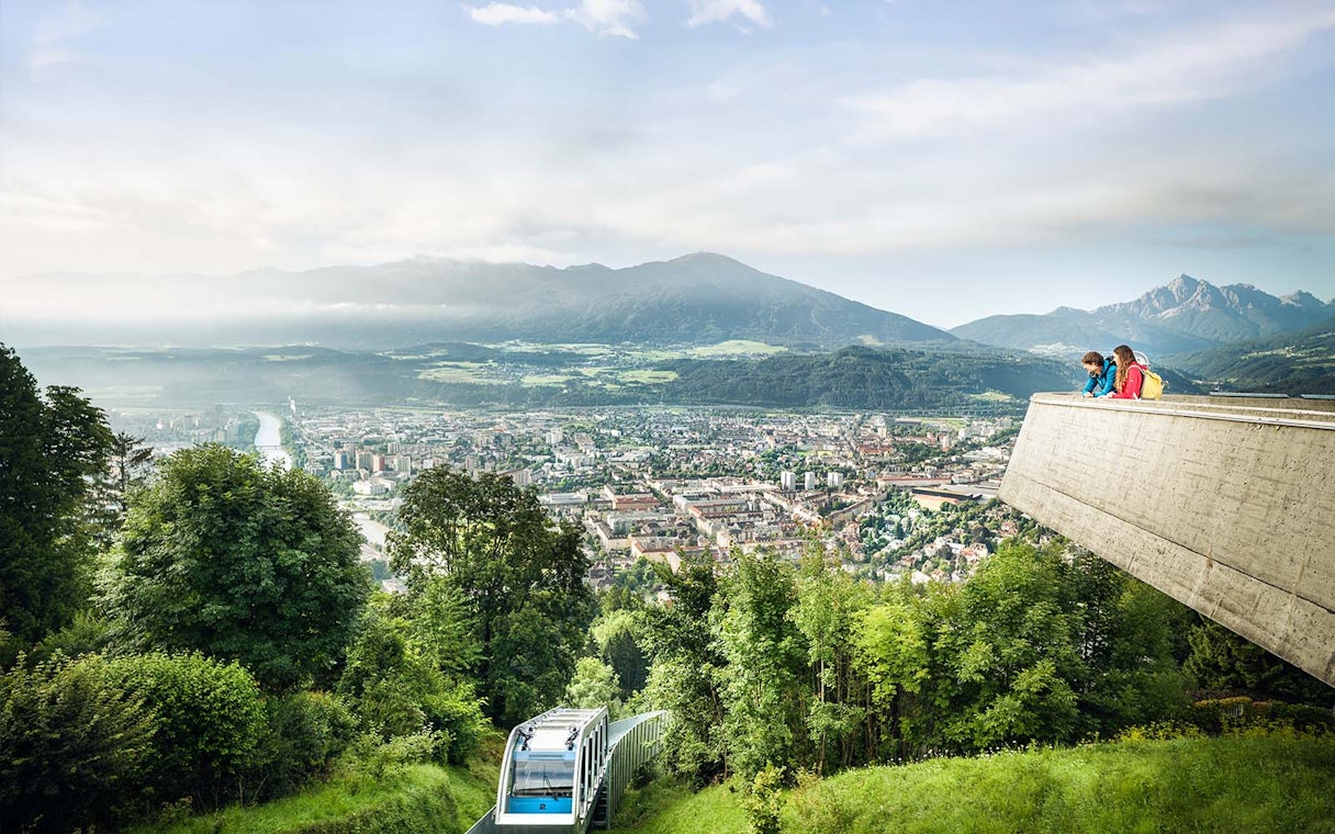 People enjoying the view from a platform overlooking Innsbruck, Austria, with a funicular below.