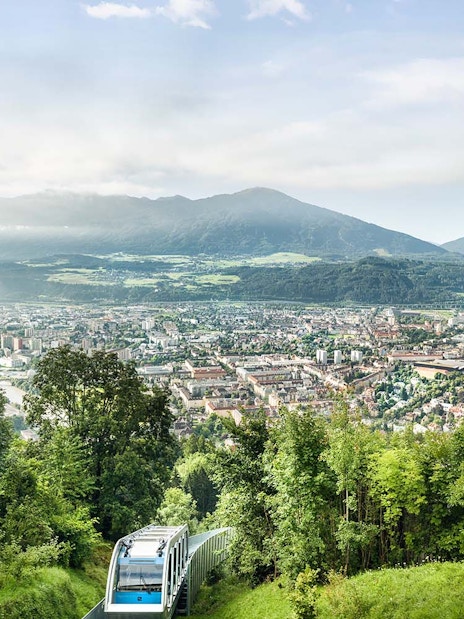 People enjoying the view from a platform overlooking Innsbruck, Austria, with a funicular below.