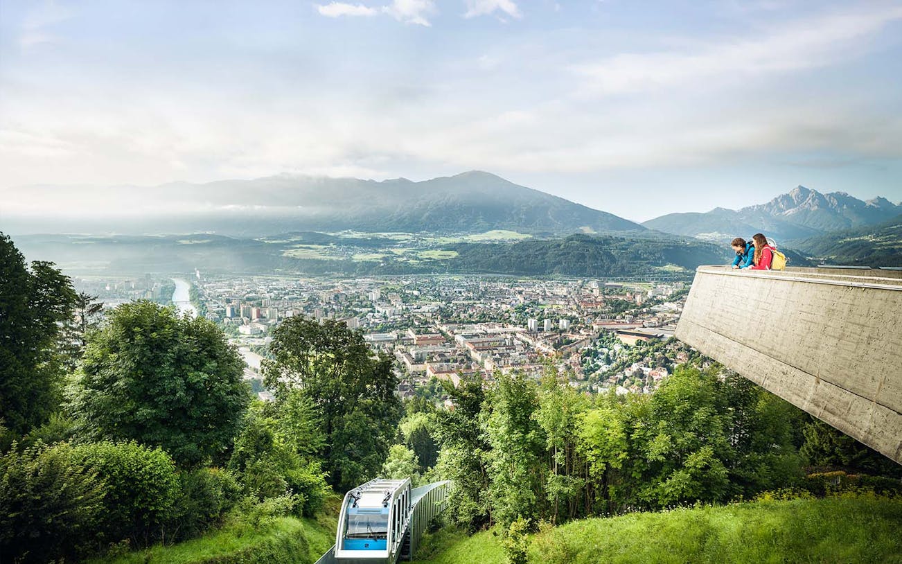 People enjoying the view from a platform overlooking Innsbruck, Austria, with a funicular below.