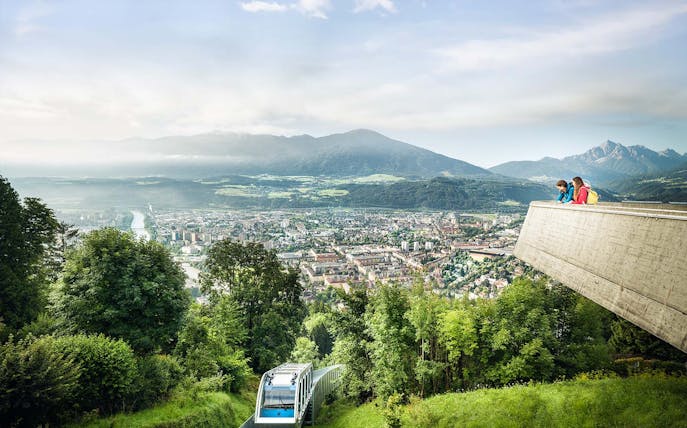 People enjoying the view from a platform overlooking Innsbruck, Austria, with a funicular below.