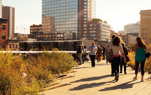 People walking along the High Line in New York City with city buildings in the background.