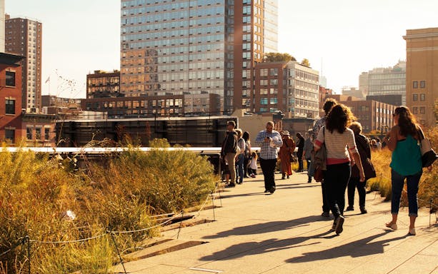 People walking along the High Line in New York City with city buildings in the background.