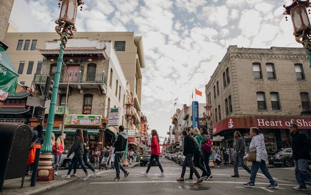 Pedestrians crossing a street in San Francisco's Chinatown, surrounded by traditional architecture and shops.