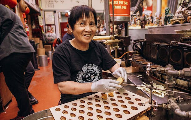 Person making fortune cookies in a Chinatown shop during the Through The Dragon Gate tour.