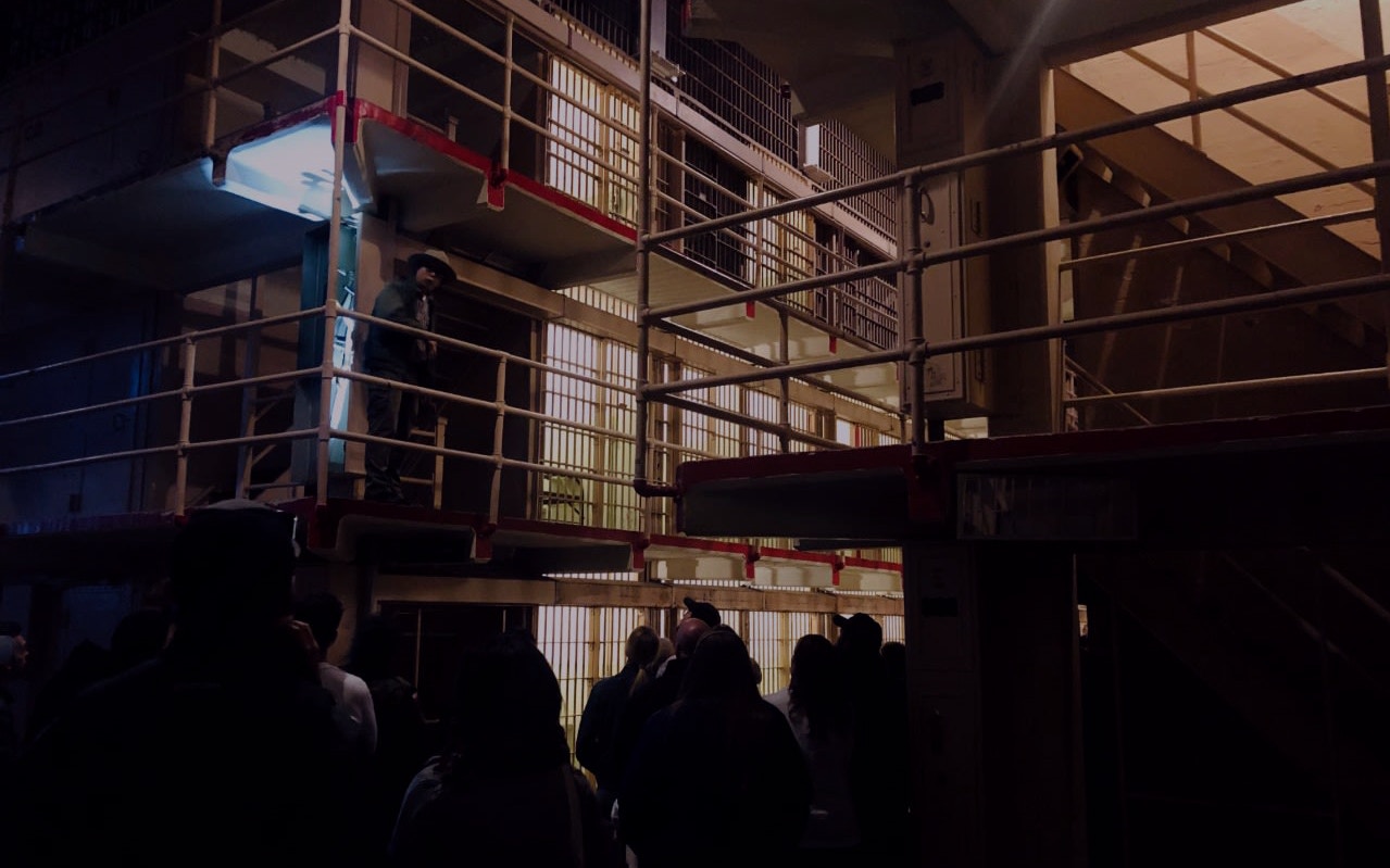 Tour group exploring Alcatraz Island cell block at night.
