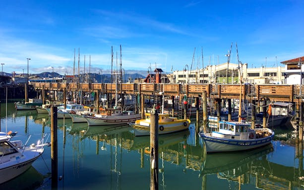 Boats docked at Fisherman's Wharf, San Francisco, with clear blue sky.