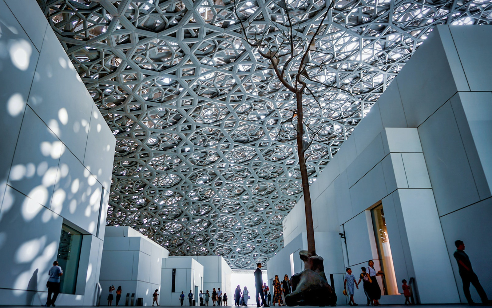 Louvre Abu Dhabi interior with geometric ceiling and visitors exploring the space.