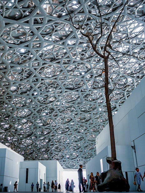 Louvre Abu Dhabi interior with geometric ceiling and visitors exploring the space.