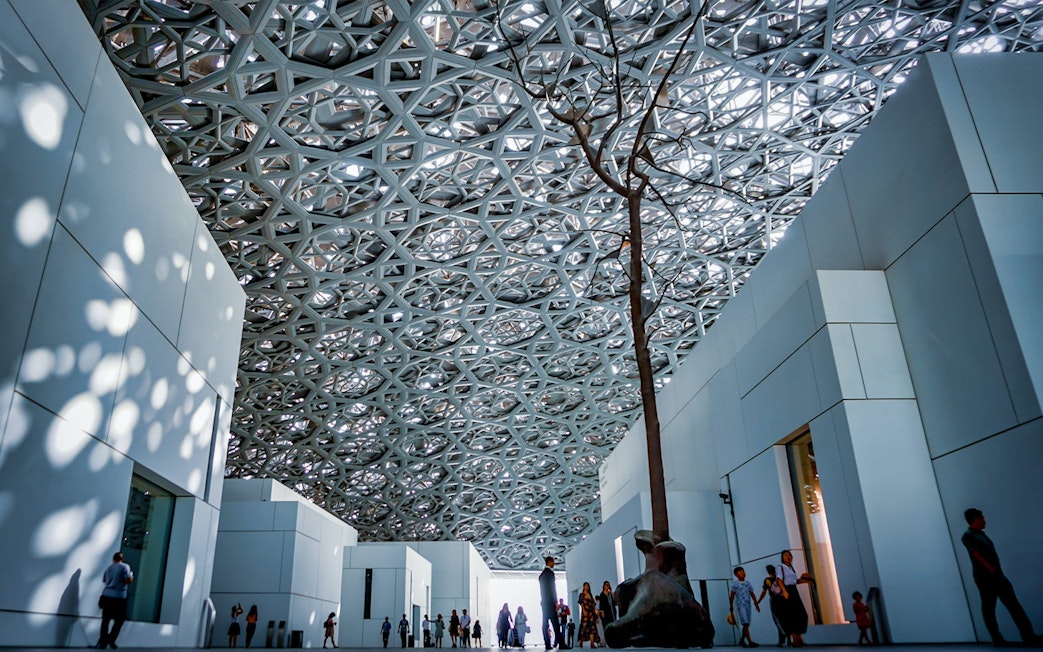 Louvre Abu Dhabi interior with geometric ceiling and visitors exploring exhibits.